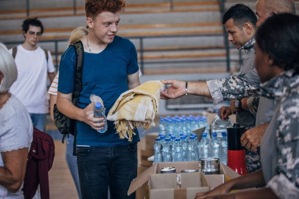 Diverse group of people, soldiers on humanitarian aid to civilians in school gymnasium, after natural disaster happened in city.